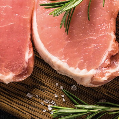 Côtelettes de porc crues avec romarin sur planche en bois.