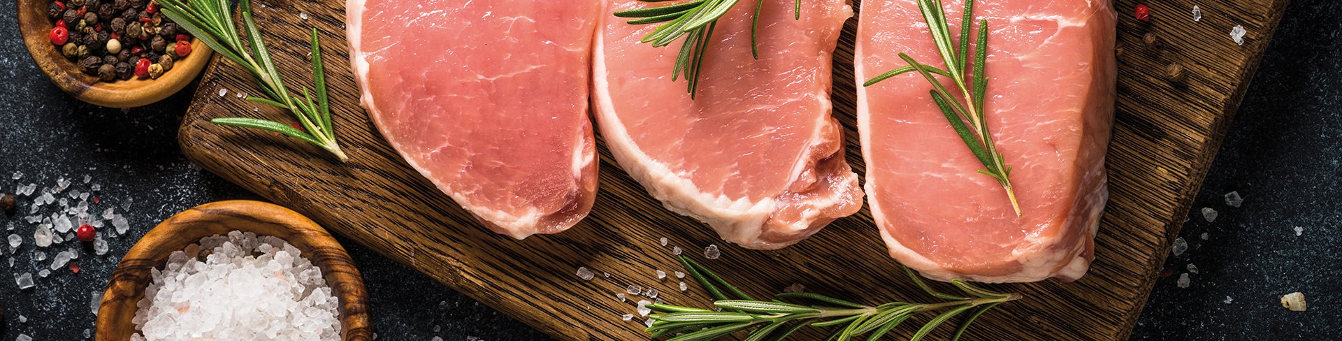 Côtelettes de porc crues avec romarin sur planche en bois.
